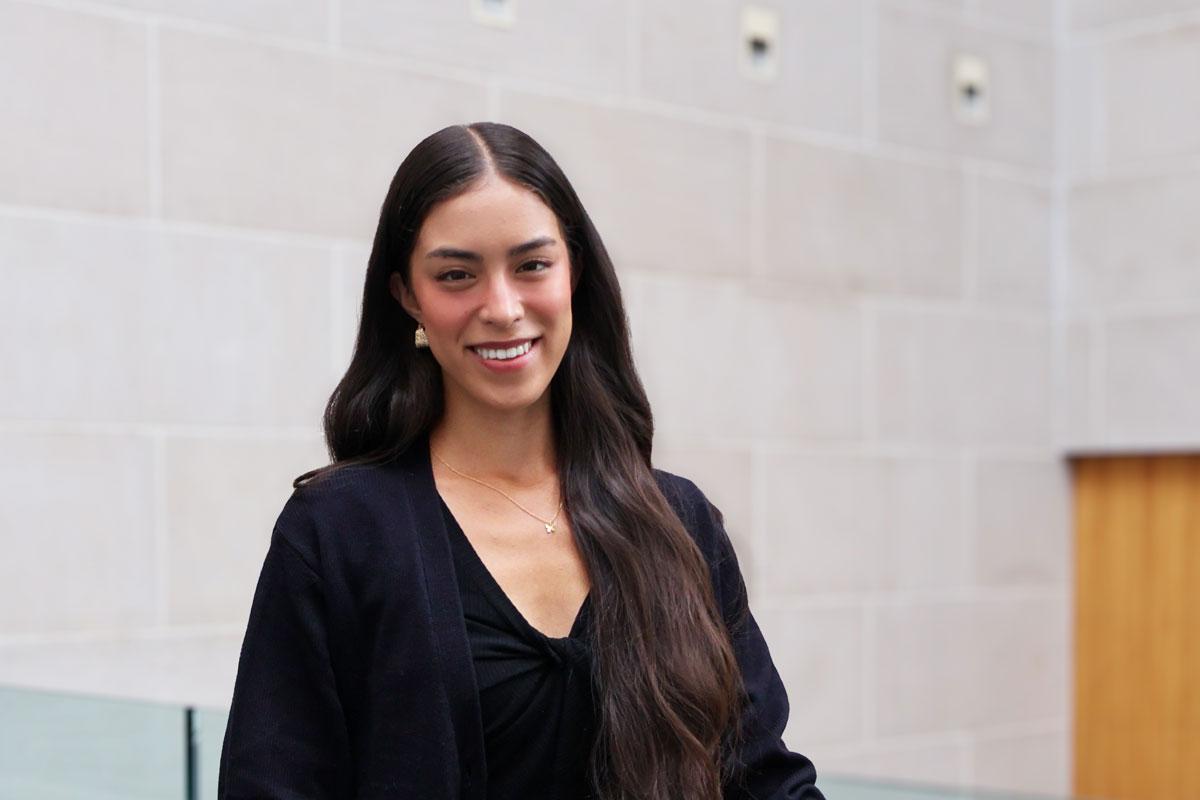 A woman with long hair in a black top smiles warmly, representing the vibrant community at the University of Rochester.